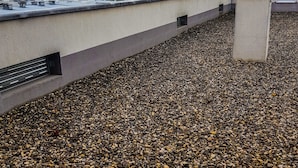 A rooftop with a pebbled surface and a modern building with a curved roof structure in the background.