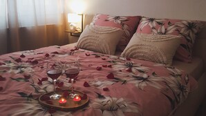 A bed with a floral bedspread, two pillows, and a tray with wine glasses and a candle.