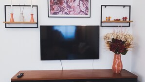 A modern living room with a flat-screen TV mounted on the wall, a wooden entertainment unit below, and two wall-mounted shelves with decorative items.