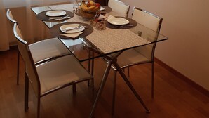 A dining area with a glass table set for four, a fruit bowl, and a wall-mounted light fixture.