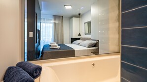 Ein modernes Hotelzimmer mit einem großen Spiegel, einem Bett, einer Badewanne und Blick auf die Stadt durch das Fenster.