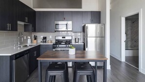 Una cucina moderna con mobili scuri, elettrodomestici in acciaio inossidabile e un tavolo in legno con due sgabelli.