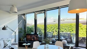 A modern living room with a large window, a round table, and a sofa. - Angel Mint Apartment (Kraków)