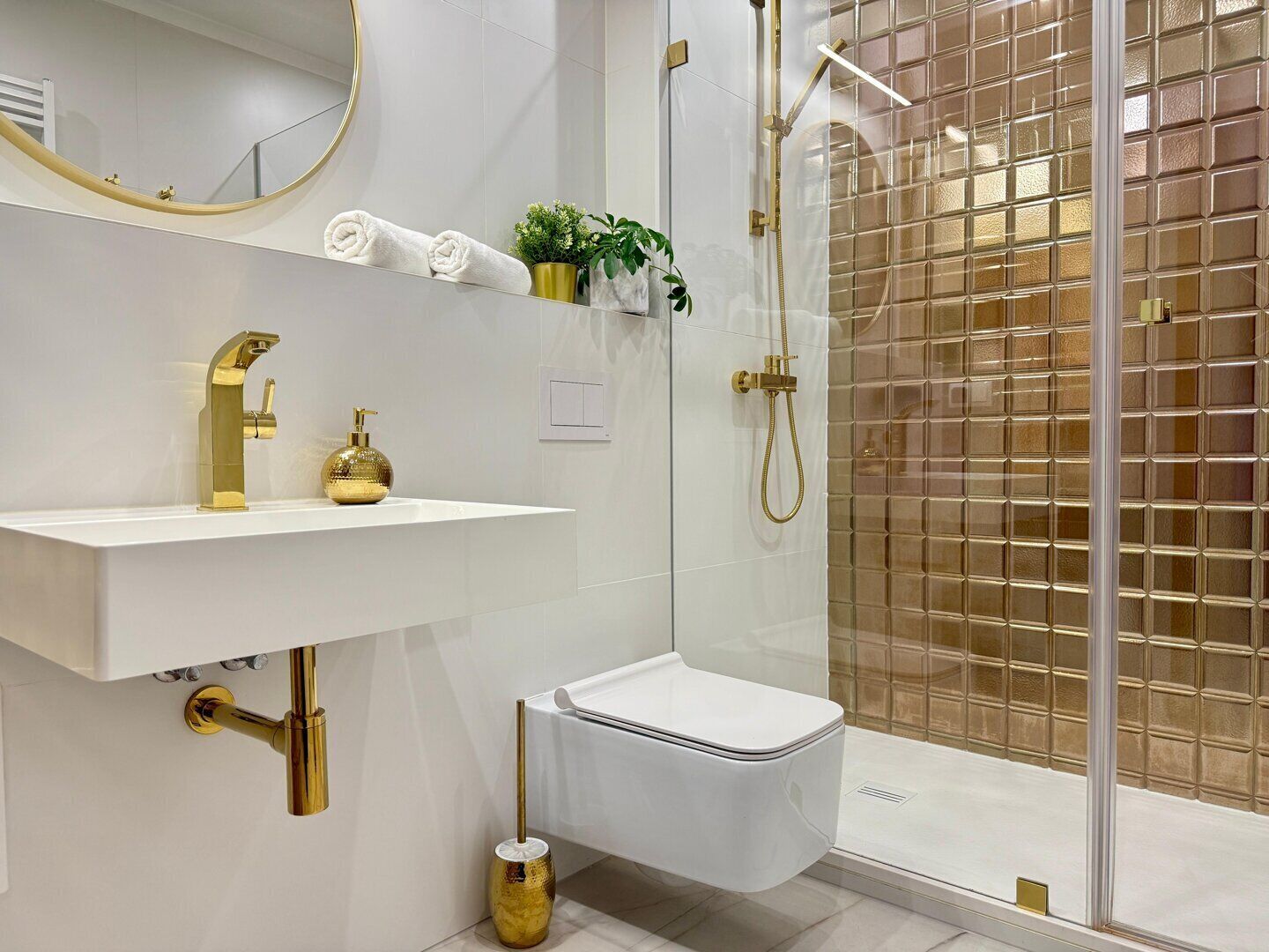 Une salle de bain moderne avec un lavabo blanc, des robinetteries dorées, une douche en verre et des toilettes blanches.