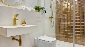 Une salle de bain moderne avec un lavabo blanc, des robinetteries dorées, une douche en verre et des toilettes blanches.