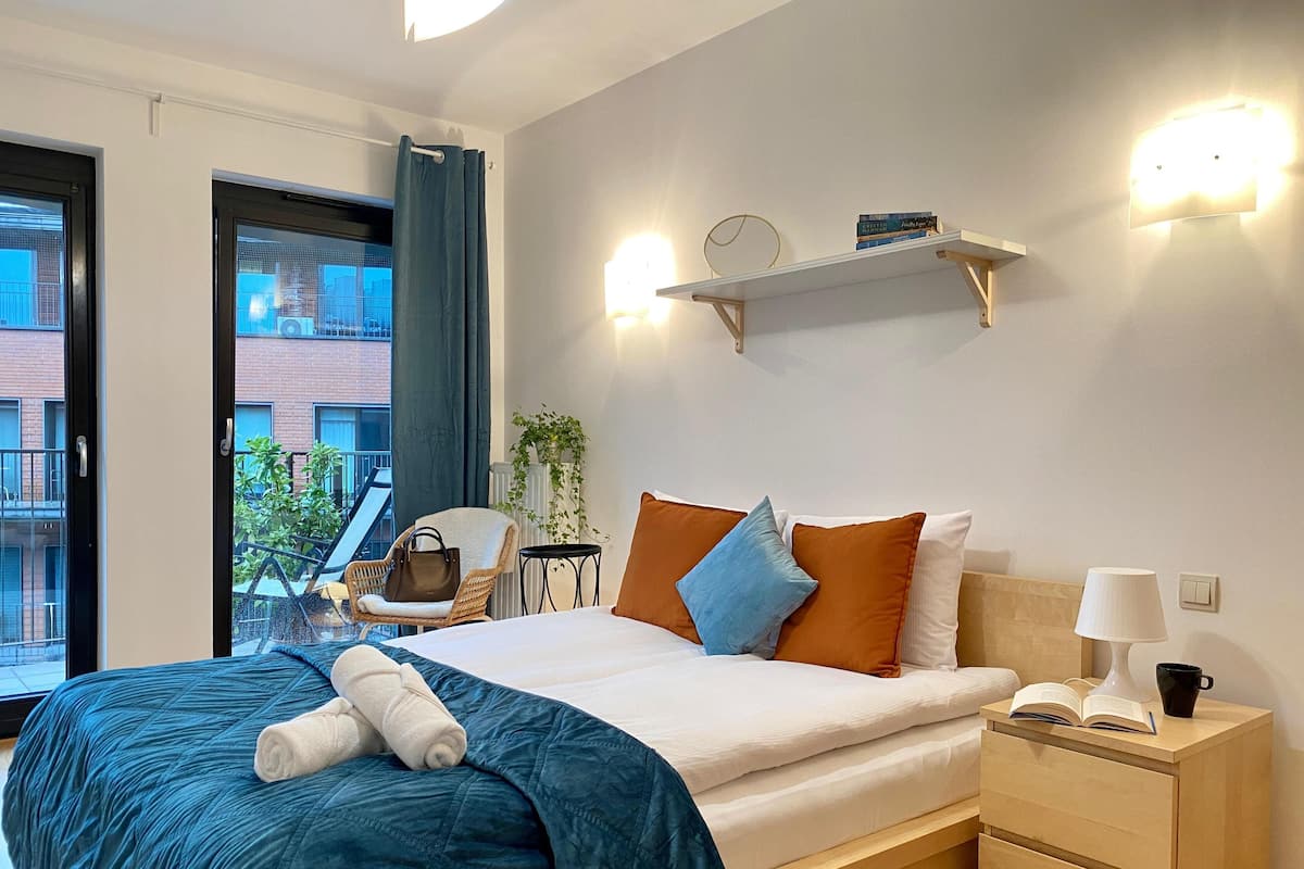 A hotel room with a bed, bedside table, and a view of the outside balcony.