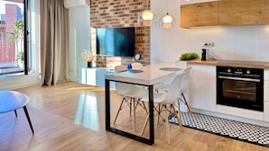 A modern kitchen with a brick accent wall, a flat-screen TV, and a dining area with a white table and chairs. - Angel Mint Apartment (Kraków)