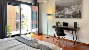 A modern bedroom with a large bed, a desk with a laptop, a potted plant, and a cityscape painting. - Angel Mint Apartment (Kraków)