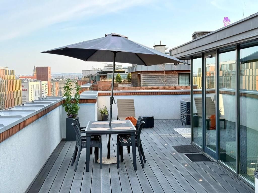 A rooftop terrace with a table and chairs, a large umbrella, and a city view.