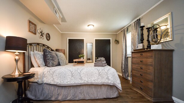 A bedroom with a bed, bedside table, dresser, and a mirror.
