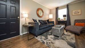 A living room with a dark door, a blue sofa, a brown armchair, a coffee table, and a rug.