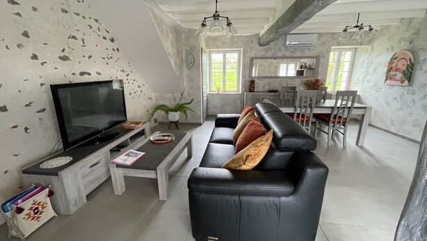 Una sala de estar moderna con un sofá de cuero negro, un televisor de pantalla plana, una mesa de centro y un comedor con una mesa y sillas blancas.
