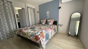 Un dormitorio con colcha estampada, un espejo de pie y suelo de madera.