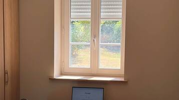 Una habitació amb escriptori, portàtil, cadira i finestra amb persianes.