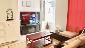 A living room with a TV displaying various streaming services, a sofa, a coffee table, and a red curtain. - Stockade Japanese Ryokan, King bed, Washer/Dryer (Schenectady)