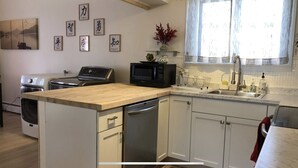 A compact kitchen with a wooden countertop, a microwave, a dishwasher, and a sink. There are cabinets and a window with a view. - Stockade Japanese Ryokan, King bed, Washer/Dryer (Schenectady)