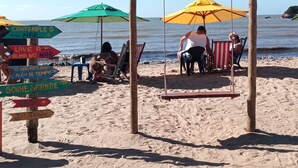 A beach with colorful umbrellas and a swing set. - Morada do Canal Búzios (Búzios)