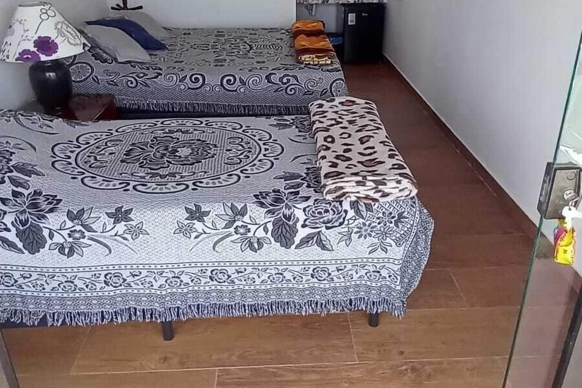A room with two beds, a small window, a TV on the wall, and a green mat at the entrance.