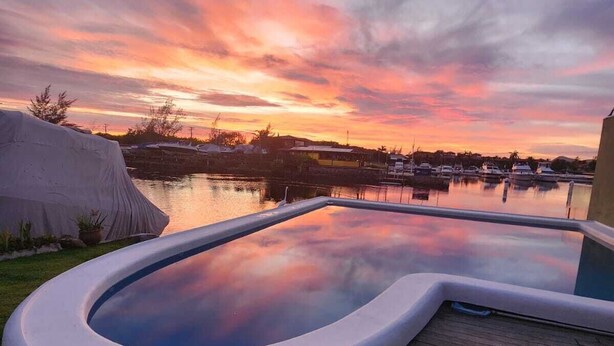 A swimming pool with a curved edge, surrounded by grass and a wooden deck. - Morada do Canal Búzios (Búzios)
