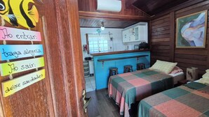 A cozy room with two beds, a small kitchenette, and a wooden door with a sign. - Morada do Canal Búzios (Búzios)