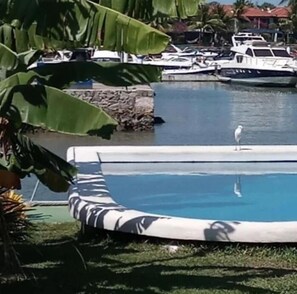 Una piscina amb una cadira de relax, un ocell al marge i vaixells al fons.