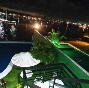 Vista nocturna d'una zona de piscina amb una font i una zona de seients coberta.