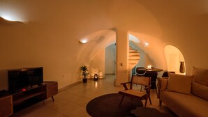 A cozy living room with a flat-screen TV, a sofa, a coffee table, and a dining area with a table and chairs. - Located at the breathtaking caldera of Imerovigli (Ημεροβίγλι)