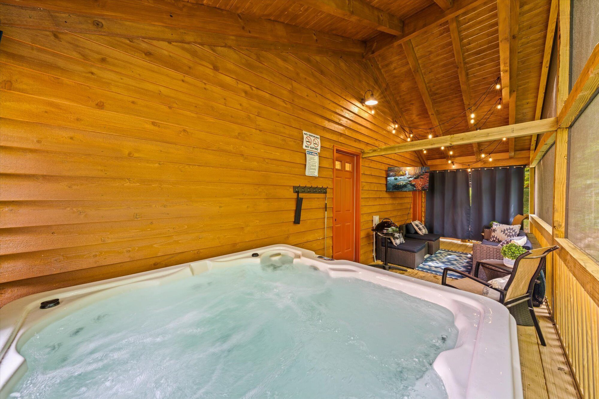 Interior de una cabaña de madera con jacuzzi, zona de estar y un cartel de prohibido fumar.