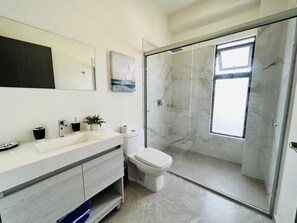 A modern bathroom with a marble shower, a large mirror, and a minimalist sink area.