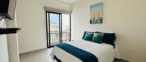 A bedroom with a bed, a ceiling fan, a painting, and a balcony with a view.