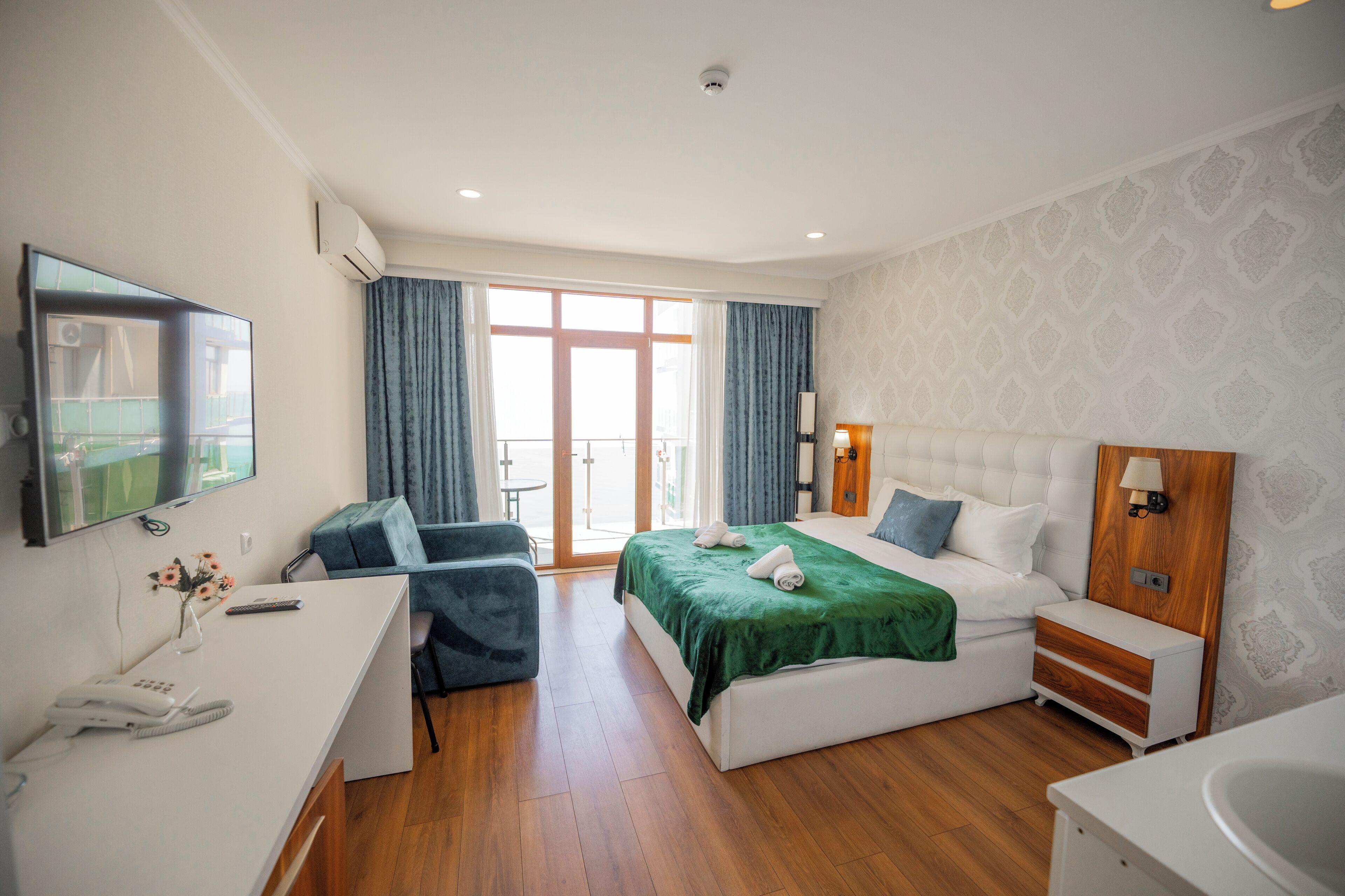 A modern hotel room with a bed, a desk, a chair, a TV, and a bathroom.