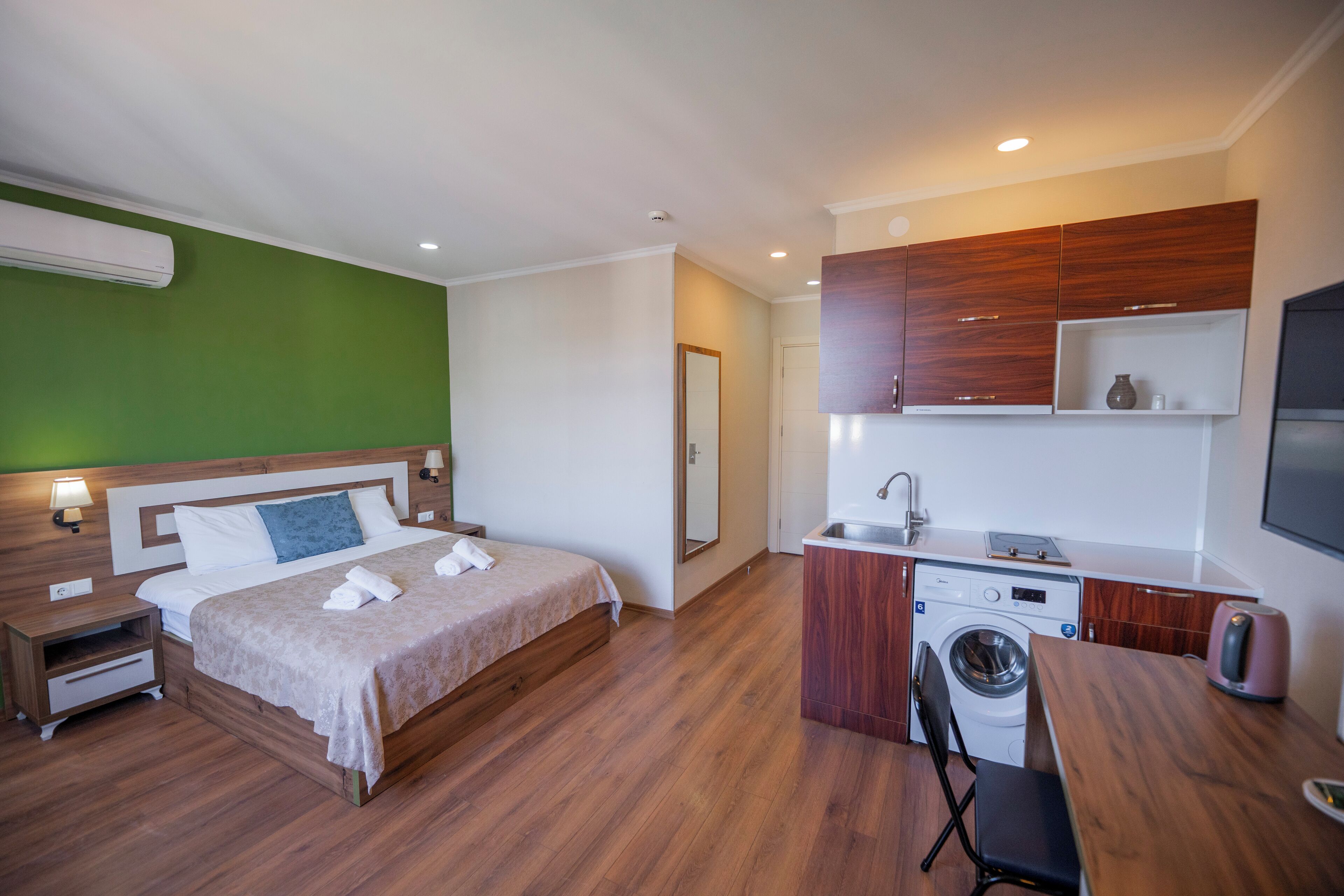 A hotel room with a bed, a small desk, a washing machine, and a kitchenette.