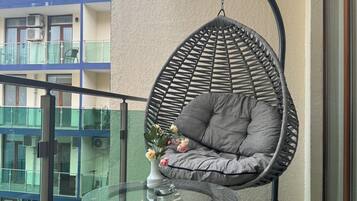 A balcony with a hanging chair, a glass table, and a vase with flowers.