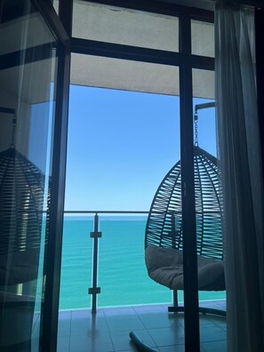 A room with a large glass window overlooking the sea, a hanging chair, and a small table. - Fresh Wave Hotel (Batumi)