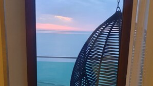 A view from a room with a large window overlooking a beach, a hanging chair, and a tiled floor. - Fresh Wave Hotel (Batumi)