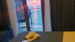 Una stanza con un letto, due asciugamani e vista sul tramonto sull'acqua.