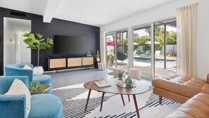Un salon moderne avec un téléviseur, des canapés et une grande fenêtre donnant sur une piscine.