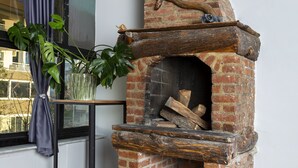 Een metselwerk schoorsteen met een houten bovenkant, een bloempot en een raam met gordijn.