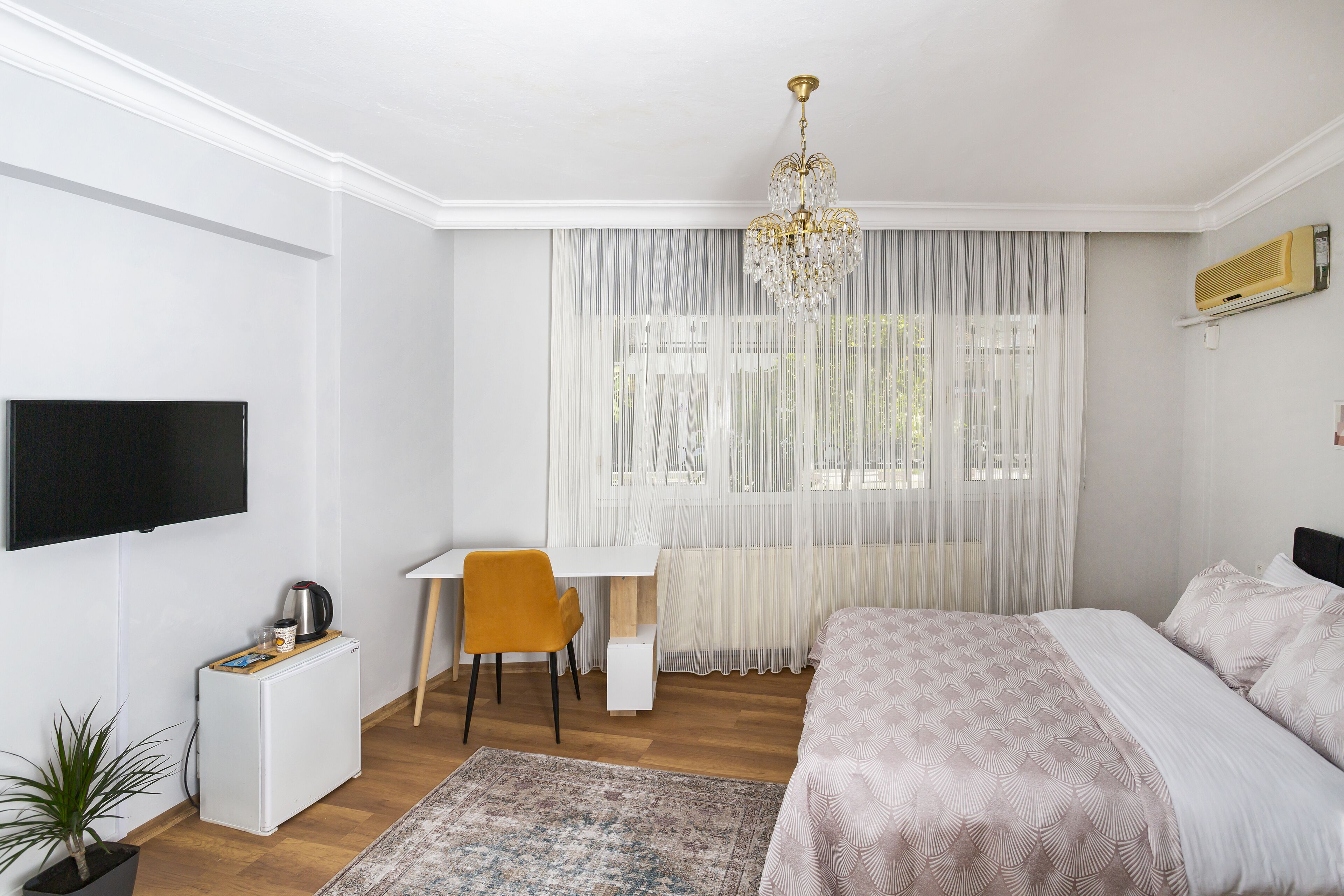 A bedroom with a bed, a desk, a chair, a TV, and a potted plant.