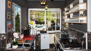 Een moderne hotellobby met een marmeren vloer, een receptiebalie, een koffieapparaat en een glazen vitrine.
