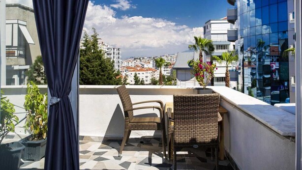 Een balkon met rieten meubilair, een potplant en uitzicht op de stad.