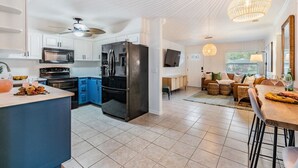 Una cocina moderna con armarios blancos, un refrigerador negro y un comedor con una mesa y sillas de madera.
