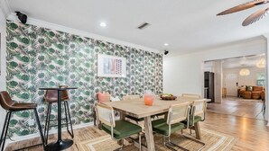 Un comedor con una mesa de madera, sillas con cojines verdes y un papel tapiz estampado.