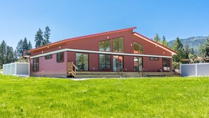Ein modernes, zweistöckiges Haus mit roter Fassade, großen Fenstern und einem Rasen.