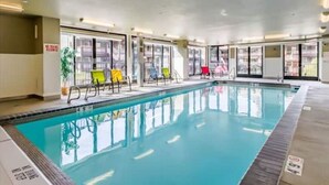 An indoor swimming pool with clear glass walls, multiple colorful lounge chairs, and a tiled floor.