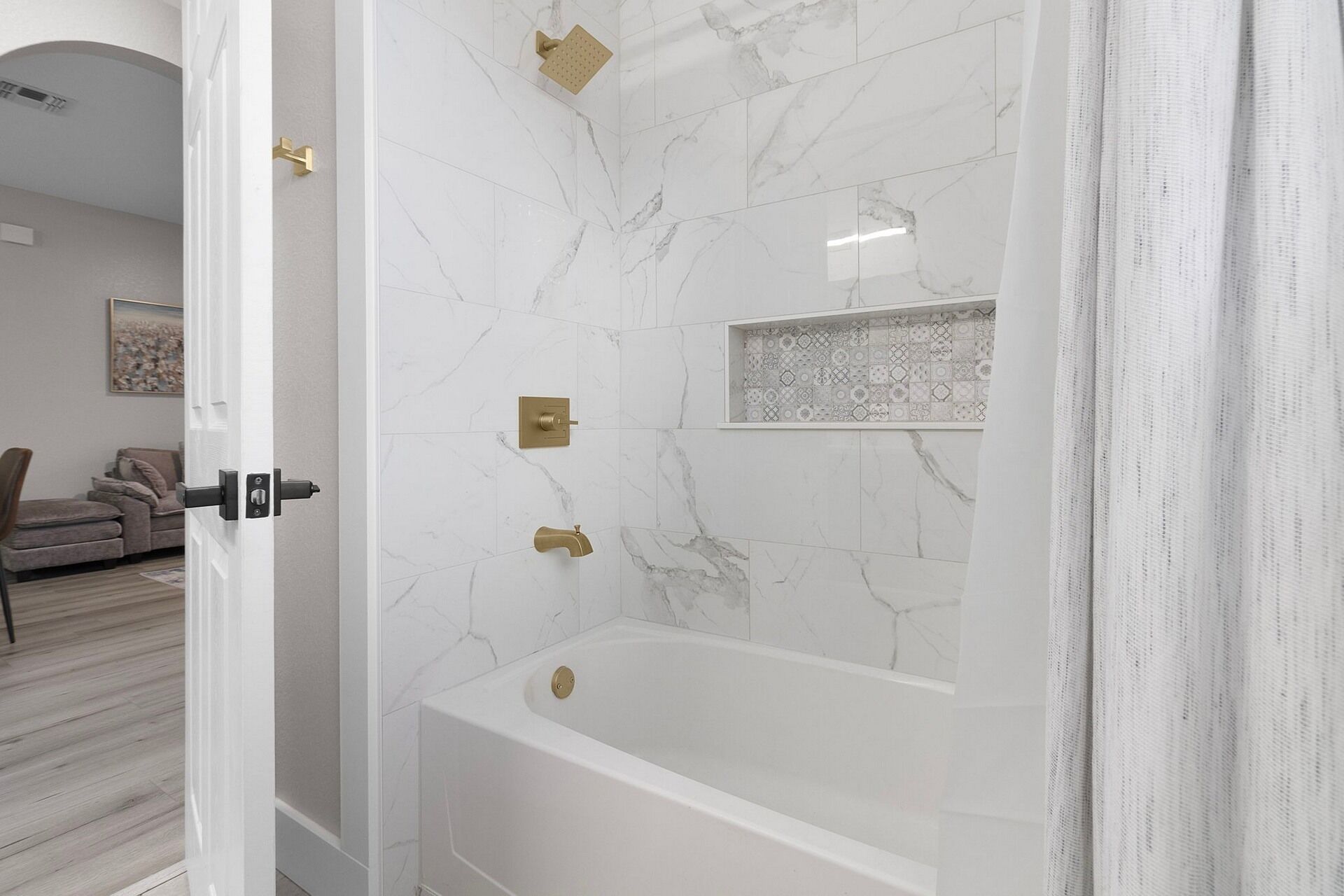Un baño moderno con pared de mármol, una bañera y una ducha con cabezal dorado.