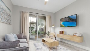 Een moderne woonkamer met een grijze bank, een houten salontafel en een aan de muur bevestigde televisie.