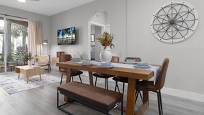 Een eetruimte met een lange houten tafel gedekt voor vier personen, omringd door stoelen. Voor de tafel staat een bank, en erboven hangt een decoratief object aan de muur.