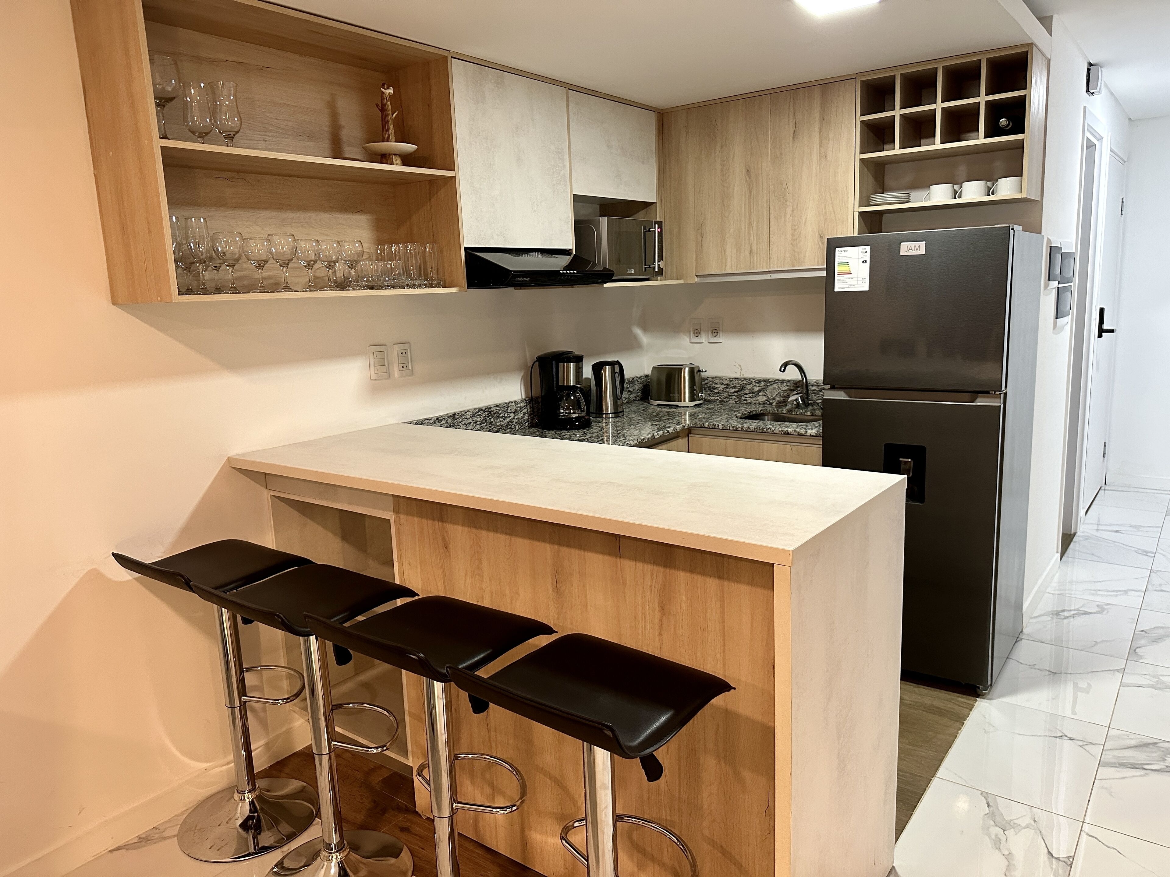 Una cocina moderna con una isla central, taburetes de bar, un refrigerador y una cafetera.