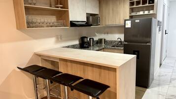 Una cocina moderna con una isla central, taburetes de bar, un refrigerador y una cafetera.
